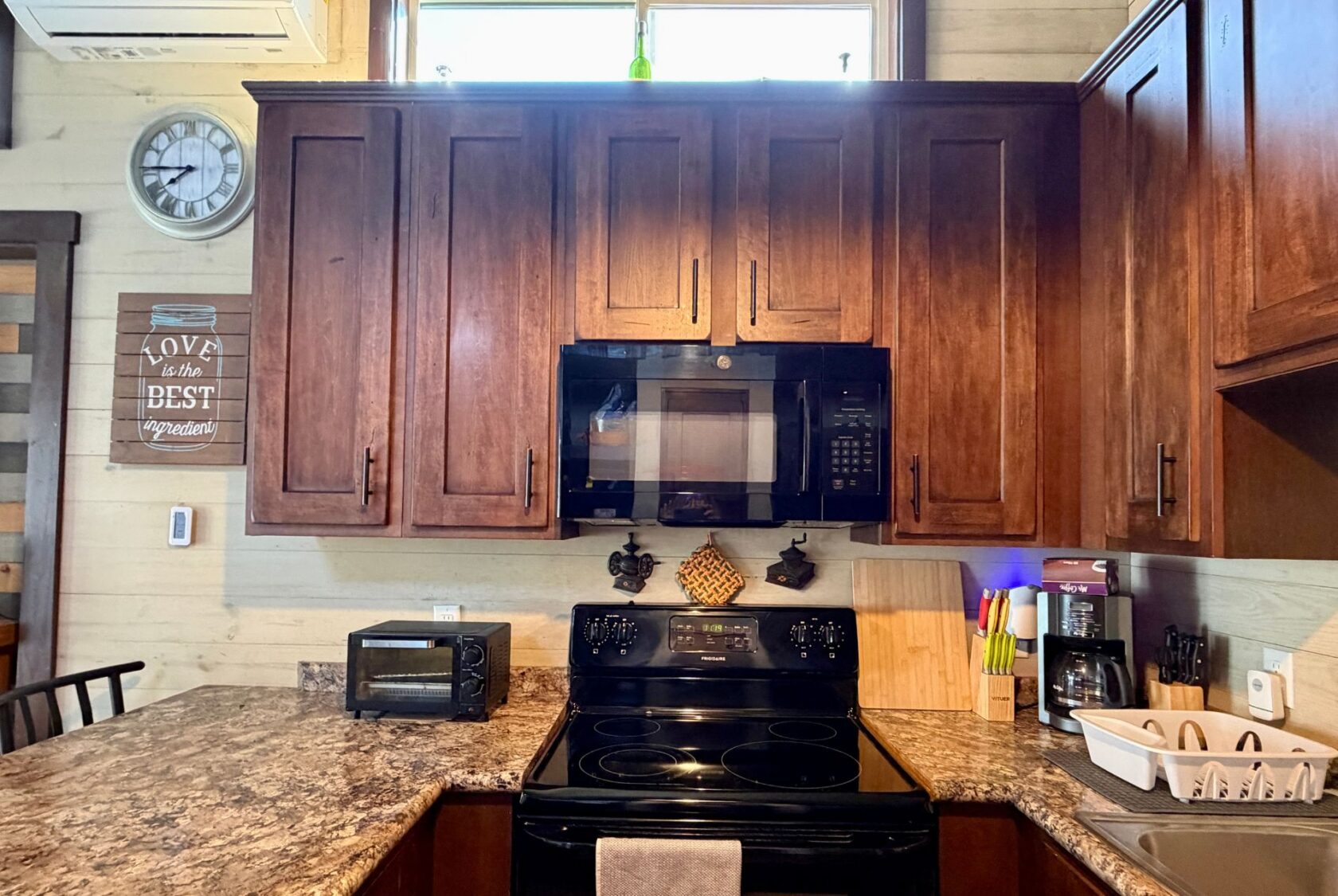 Modern kitchen on Rest Awhile Lane with dark wood cabinets, black stove, countertop appliances, and wall clock.