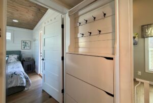 Hallway at Mount Meadow Lane with hook rack and dresser, leading to a bedroom with shiplap walls and wood ceiling.