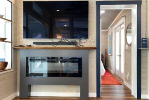 A modern living room on Just Wandering Lane features a wall-mounted TV above an electric fireplace and a bright bedroom doorway.