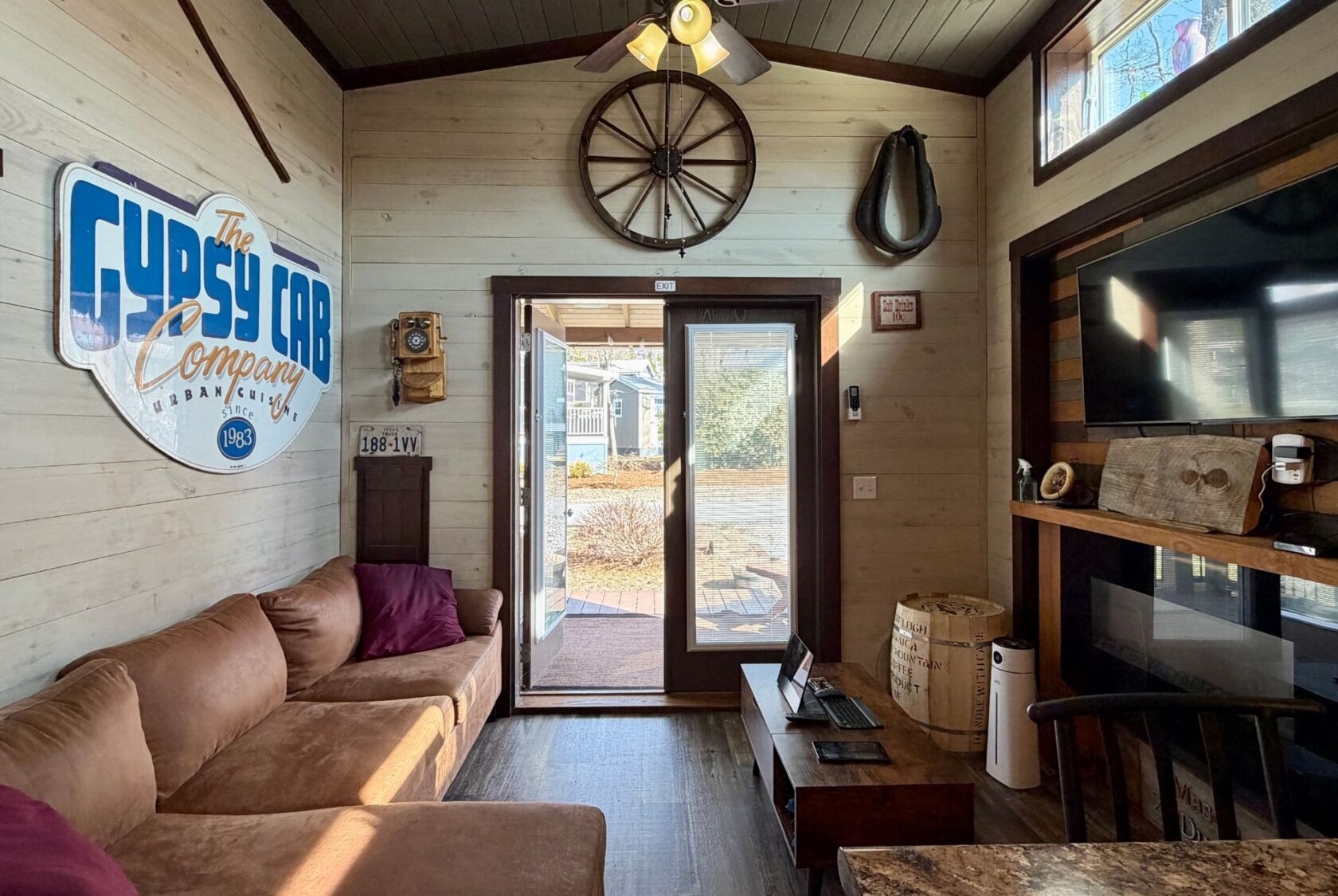 Cozy, rustic living room with brown couches, wooden decor, and a large Rest Awhile Lane sign by sunlit glass doors.