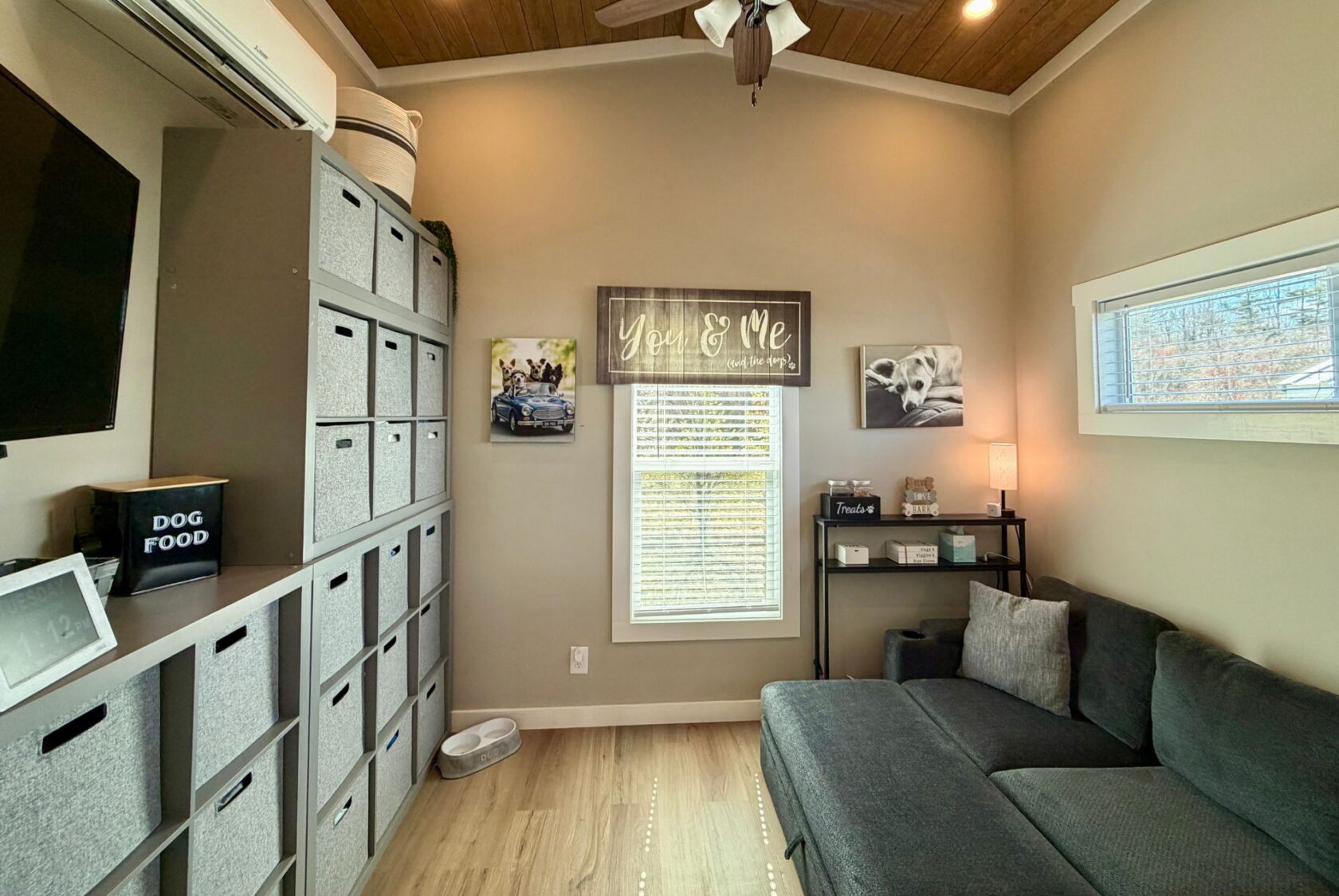 A cozy Mount Meadow Lane room with gray storage bins, a dark sofa, wall art, and a naturally lit window.