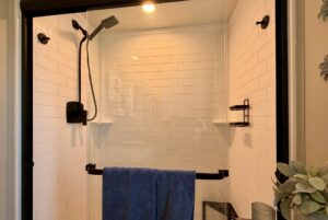 Modern shower on Mount Meadow Lane with white subway tile, black fixtures, glass door, and a blue towel on the handle.