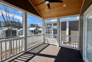 Screened porch with wooden ceiling and fan, overlooking real estate on Breezy Meadow Lane under a blue sky.