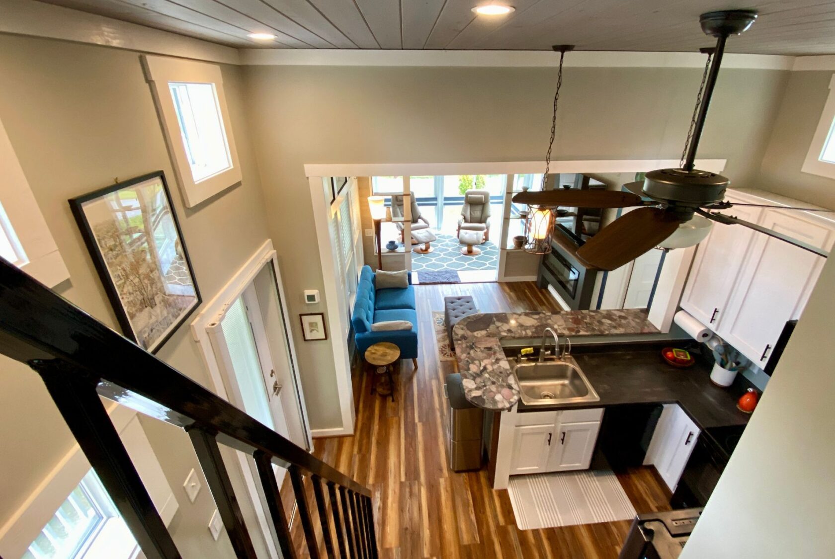View of a modern tiny house interior on Just Wandering Lane, with kitchen, living area, wood floors, and bright light.