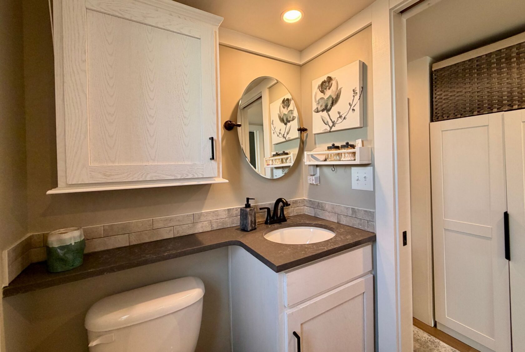 Modern bathroom on Mount Meadow Lane with white cabinets, round mirror, and floral wall art above a dark countertop.