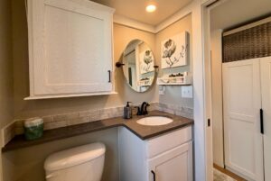 Modern bathroom on Mount Meadow Lane with white cabinets, round mirror, and floral wall art above a dark countertop.