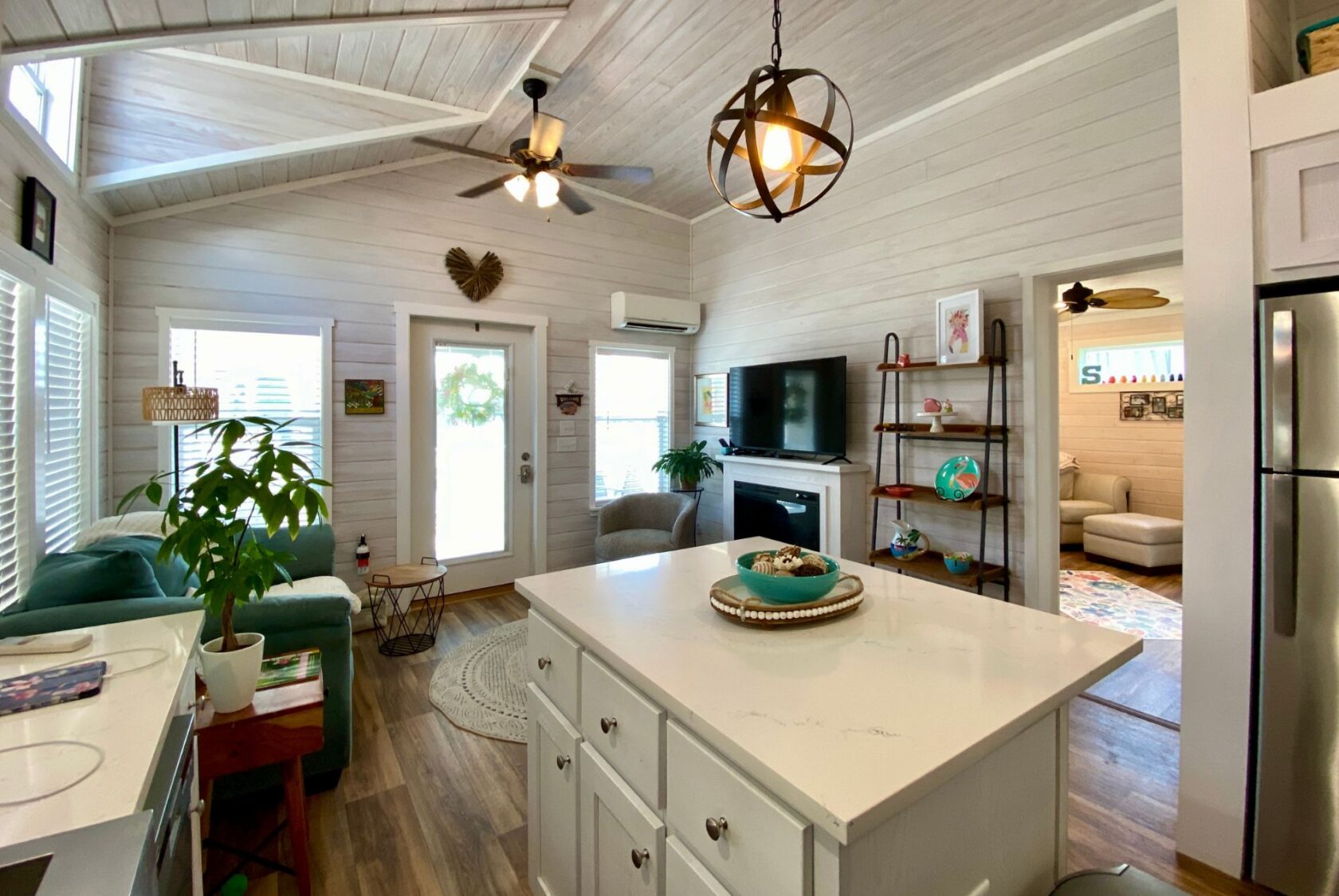 Bright, cozy living space on Strolling Easy Lane with a kitchen island, green sofa, TV, fan, and natural light.