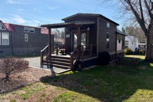 A small brown cabin at 31 Rest Awhile Lane features a porch, picnic table, and chairs on a sunny grassy lawn.