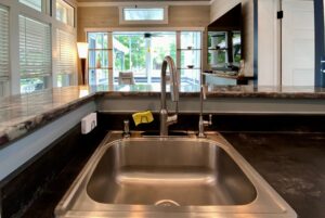 Close-up of a kitchen sink with a modern faucet at Just Wandering Lane, overlooking a bright living area with large windows.