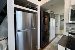 Modern kitchen on Mount Meadow Lane with a stainless steel fridge, stacked washer and dryer, and light wood cabinetry.