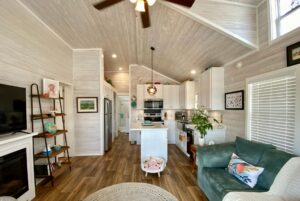 Bright, modern living room and kitchen with wood accents, teal sofa, and a Strolling Easy Lane vibe.