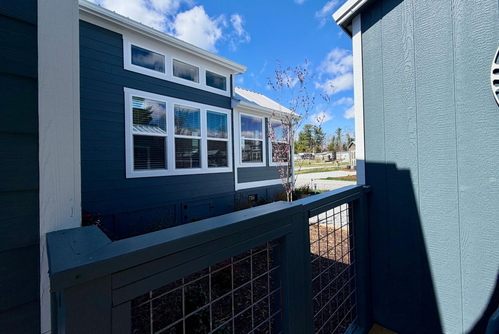 View from a porch with blue railing on Mount Meadow Lane, looking at a blue house with white trim under a partly cloudy sky.