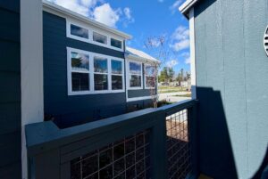 View from a porch with blue railing on Mount Meadow Lane, looking at a blue house with white trim under a partly cloudy sky.