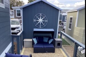 Small patio on Mount Meadow Lane with navy cushioned seating, nautical compass wall art, and gravel ground between tiny houses.