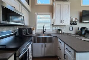 Modern kitchen on Mount Meadow Lane with white cabinets, black countertops, and a large farmhouse sink.