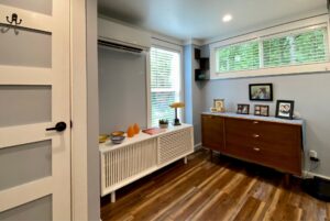 Bright, modern room on Just Wandering Lane with wood floors, dresser, decor, family photos, and large windows with blinds.