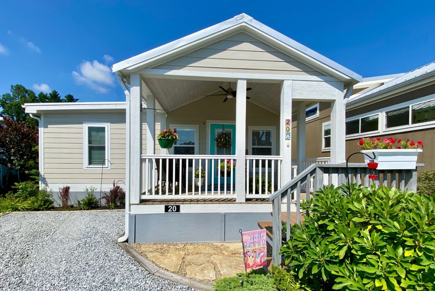 A small beige house on Easy Lane with a front porch, flowers, and a ramp, perfect for strolling on a sunny day.