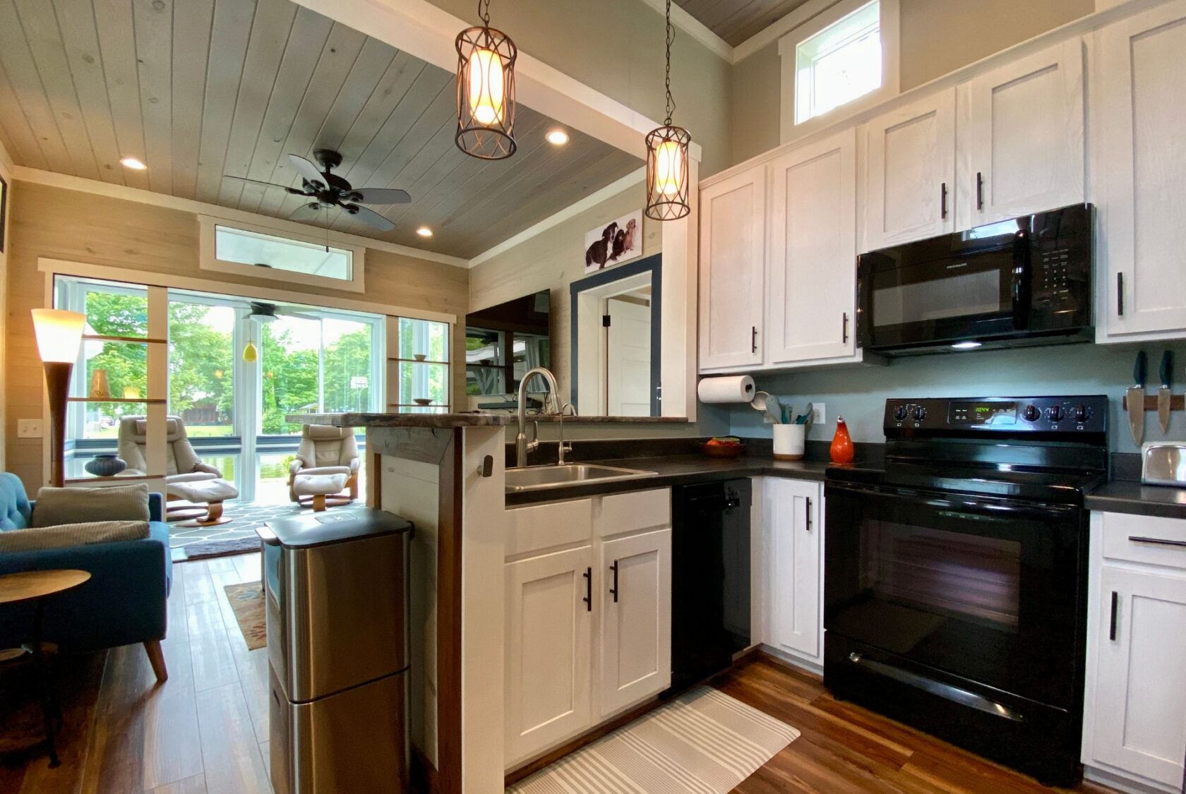 Modern kitchen with white cabinets, black appliances, and open view to a bright Just Wandering Lane living area.