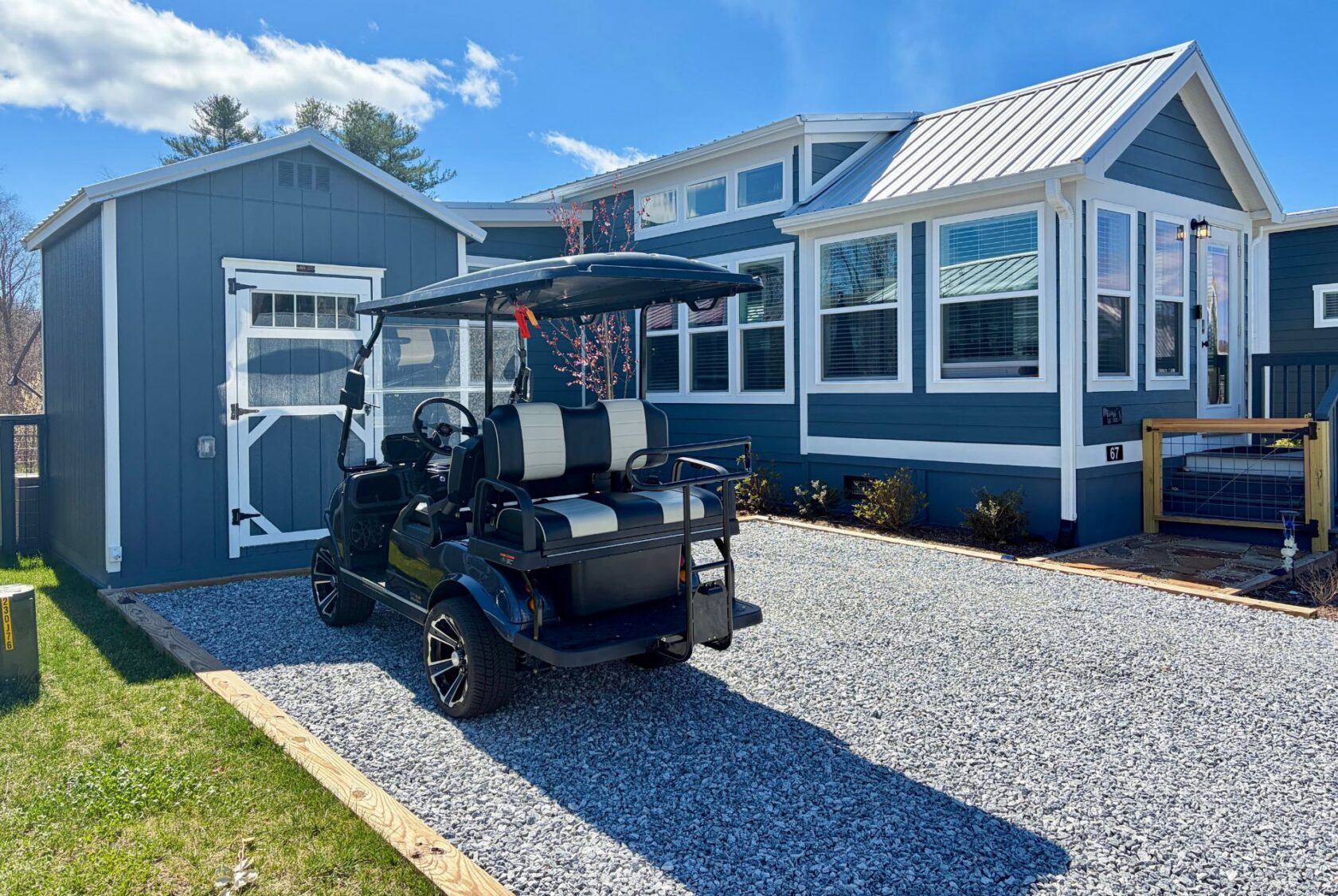 A black golf cart is parked on Mount Meadow Lane in front of a modern blue tiny house with white trim.