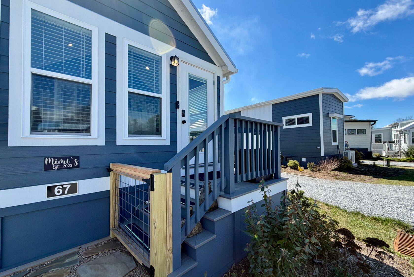 Blue tiny house with white trim, front porch, and steps on Mount Meadow Lane; another tiny house in the background.
