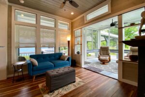 Bright, cozy sunroom on Just Wandering Lane with blue sofa, large windows, wood floors, and patio views.