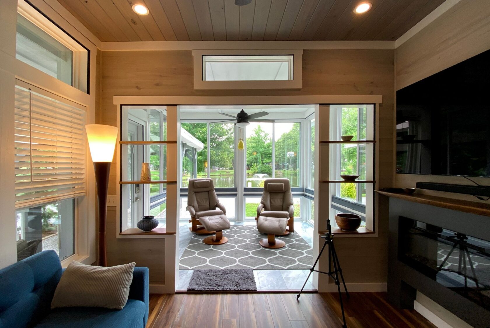 Cozy sunroom on Just Wandering Lane with recliners, rugs, shelves, and large windows overlooking green scenery.
