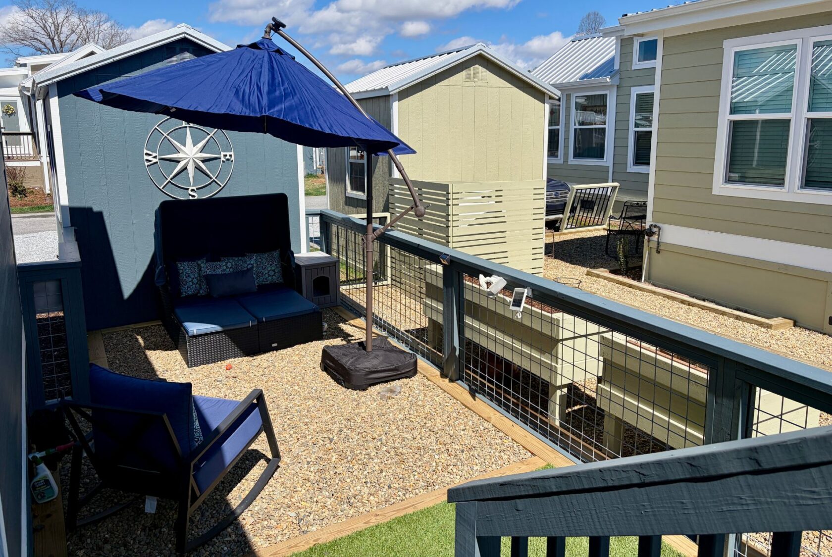 Cozy outdoor patio with seating, umbrella, and gravel ground on Mount Meadow Lane between modern tiny homes.