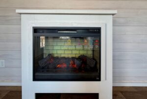 White electric fireplace with faux logs and glowing embers, featured in real estate at 119 Breezy Meadow Lane.