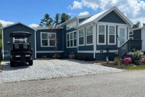 A modern blue tiny house with white trim sits on Mount Meadow Lane, featuring a porch and a golf cart on the driveway.