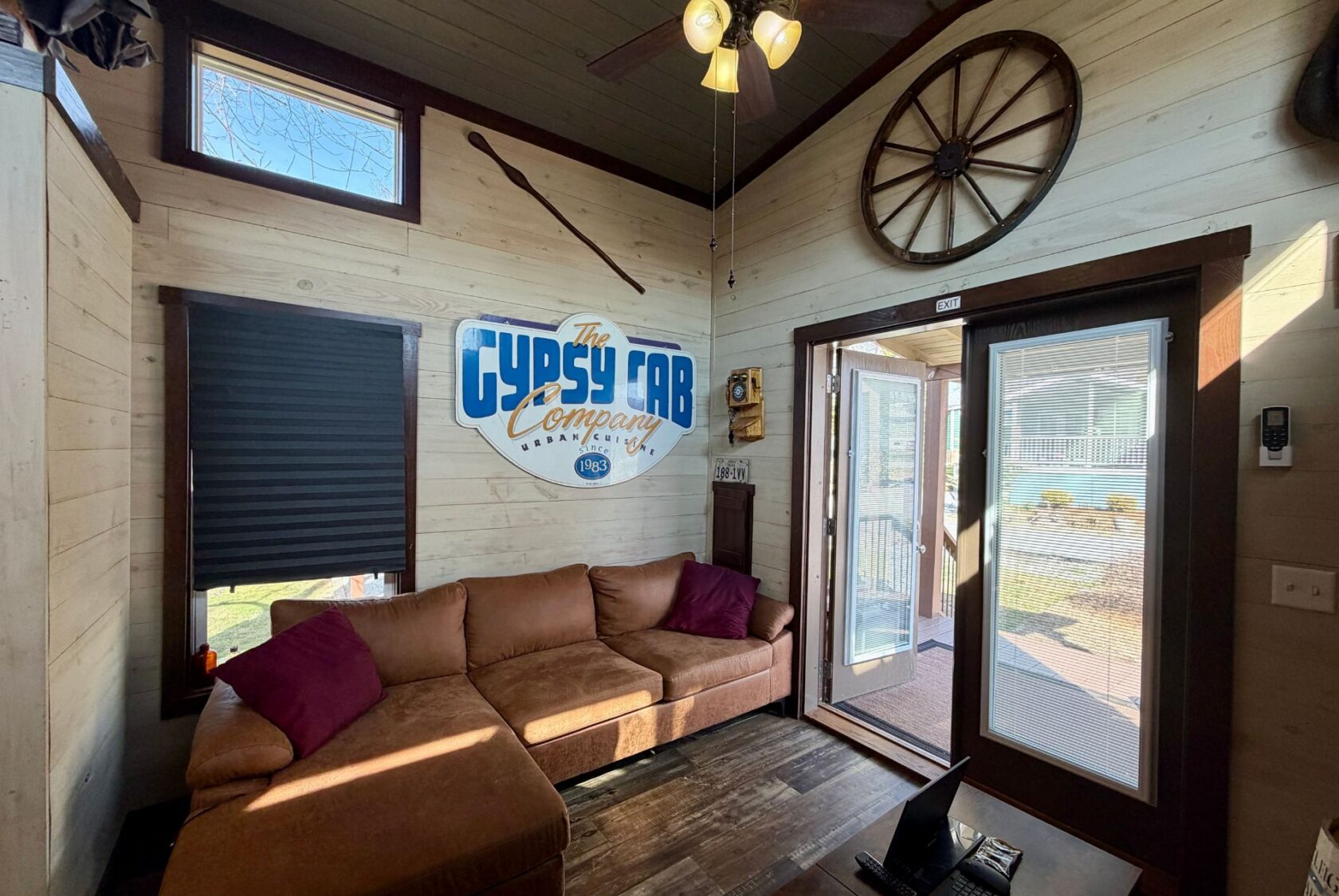 Cozy living room at 31 Rest Awhile Lane with tan sofa, wall art, wagon wheel decor, and sunlight through open glass door.