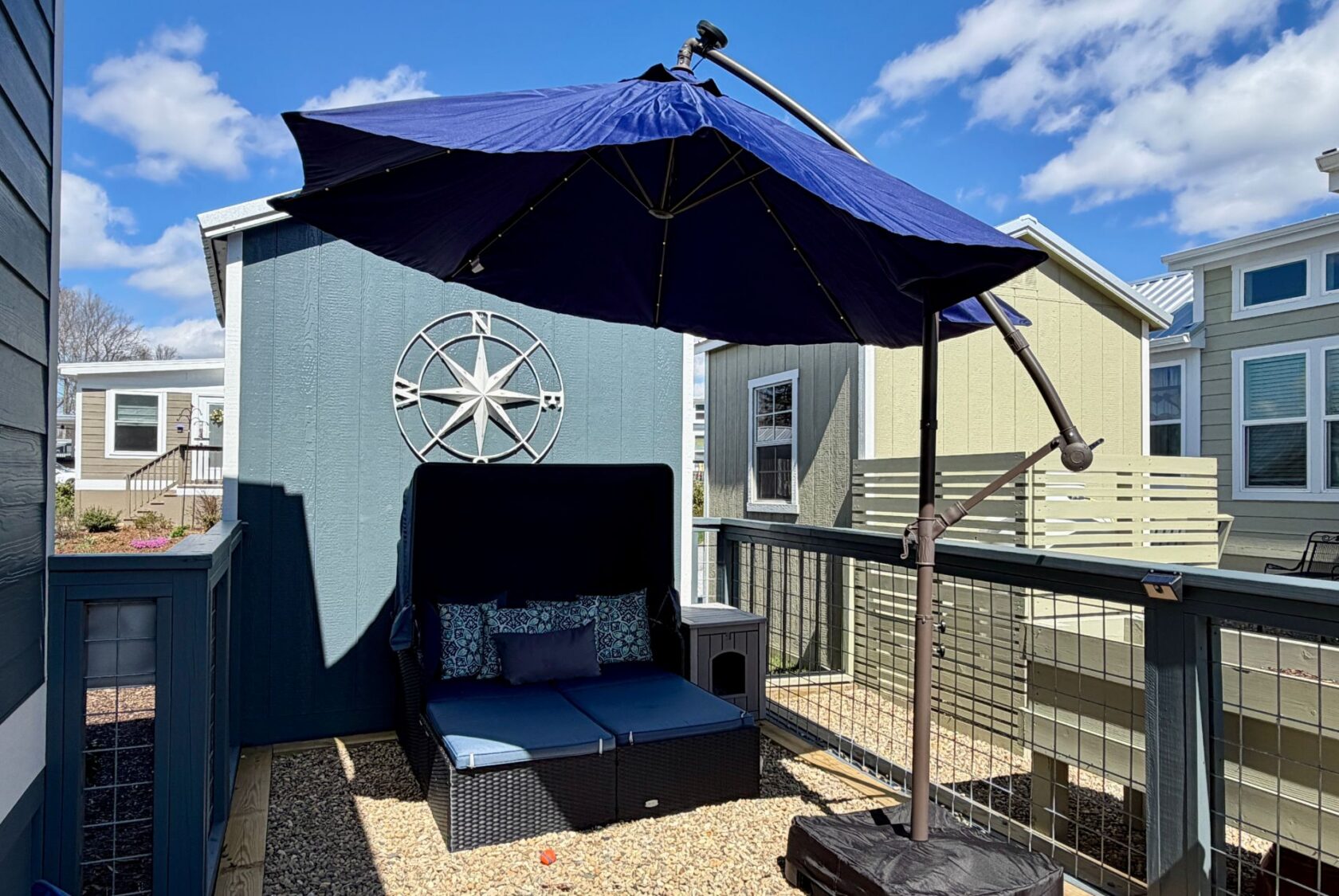 A cozy Mount Meadow Lane patio with a blue umbrella, cushioned seating, and a shed featuring a compass decoration.