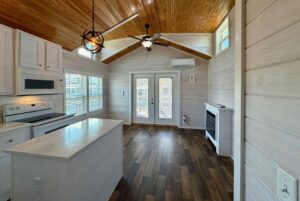 Tiny house interior at 119 Breezy Meadow Lane with wood floors, white kitchen, vaulted ceiling, and double glass doors.