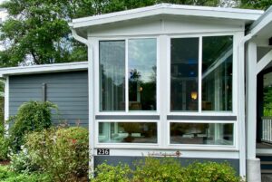 Modern house with large glass windows on Just Wandering Lane; gray siding, lush green plants, and house number 236.
