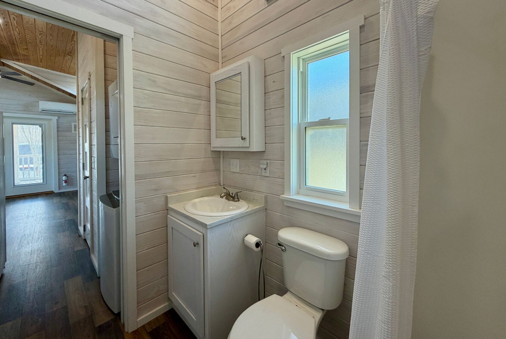 Small bathroom on Breezy Meadow Lane with sink, cabinet, toilet, window, shower, and wooden walls and floor.