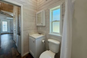 Small bathroom on Breezy Meadow Lane with sink, cabinet, toilet, window, shower, and wooden walls and floor.