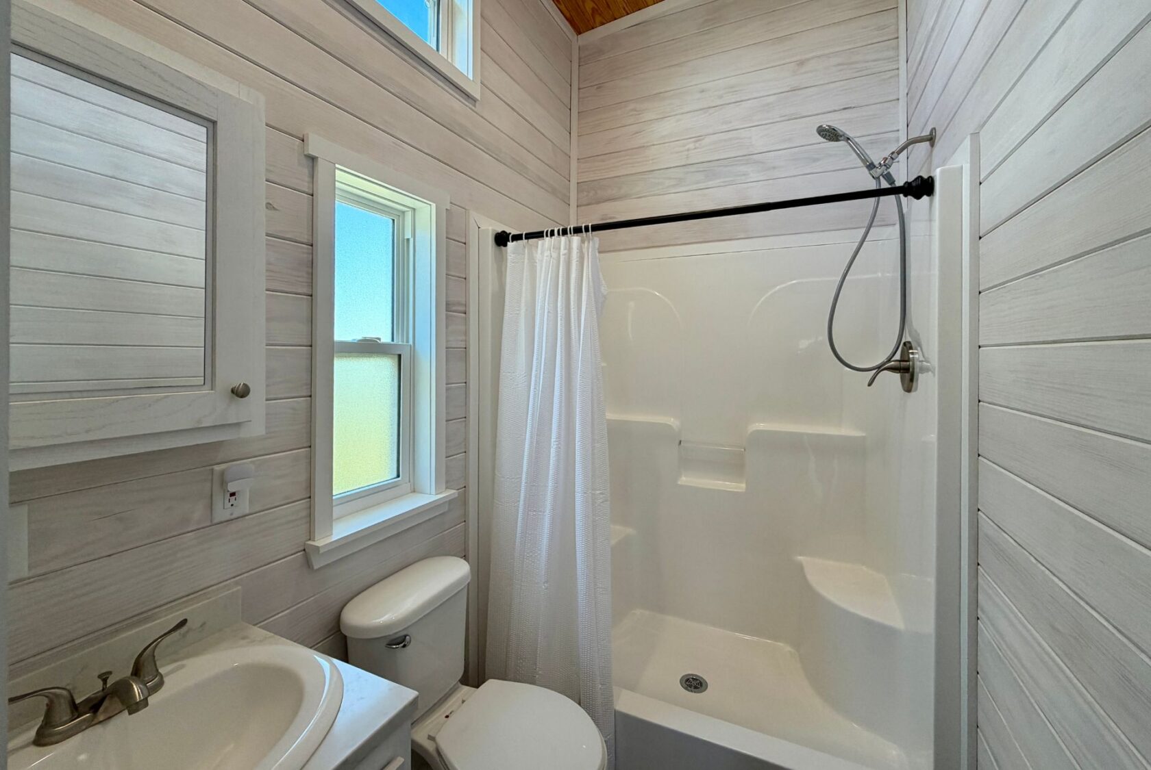 Charming small bathroom at 119 Breezy Meadow Lane with white wood walls, shower, toilet, sink, and window—ideal real estate!