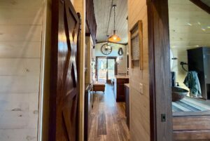 View of a cozy, rustic tiny house on Rest Awhile Lane with wooden walls, barn door, and kitchen leading to the living area.