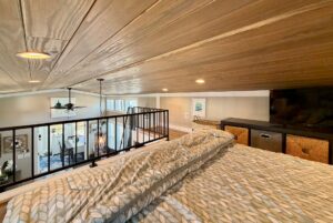 View from a loft bed on Mount Meadow Lane overlooking a modern, open living space with wood ceiling and black railing.