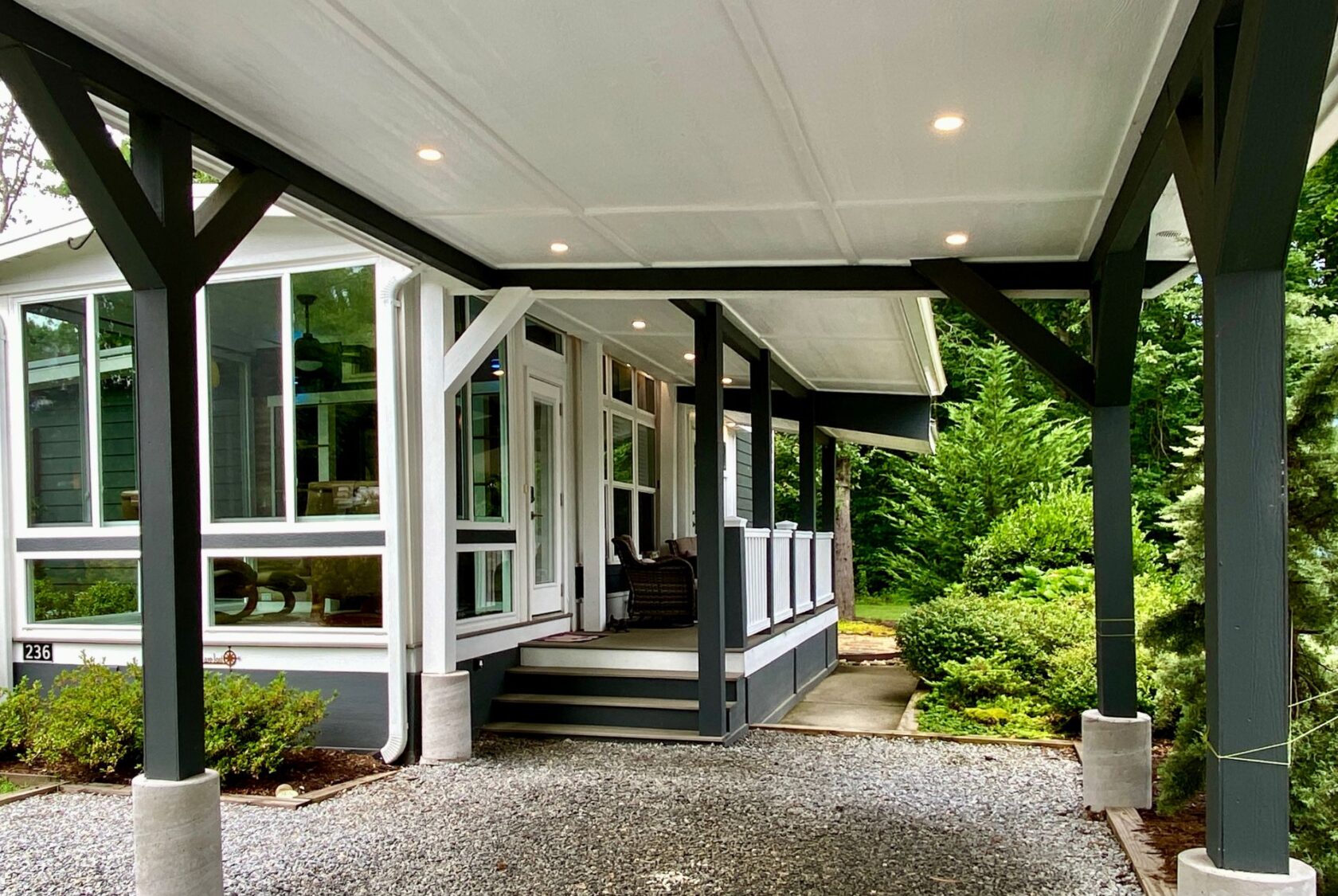 Covered porch with modern columns and seating, surrounded by greenery on peaceful Just Wandering Lane.