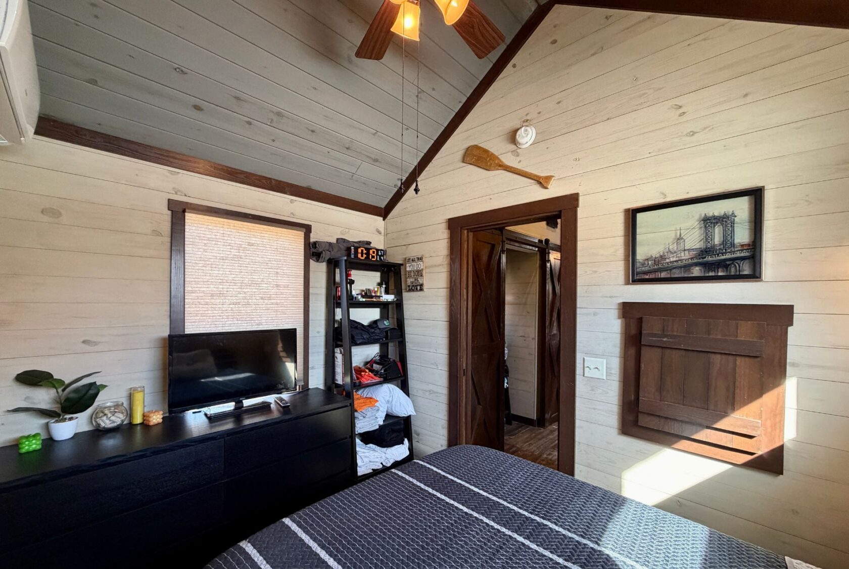 Cozy bedroom at 31 Rest Awhile Lane with wood-paneled walls, TV, dresser, open closet, wall art, and ceiling fan.