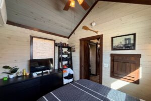 Cozy bedroom at 31 Rest Awhile Lane with wood-paneled walls, TV, dresser, open closet, wall art, and ceiling fan.