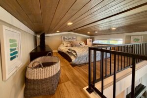 Cozy loft bedroom at 67 Mount Meadow Lane with wood ceiling, bed, small TV, wicker basket, and framed wall art.