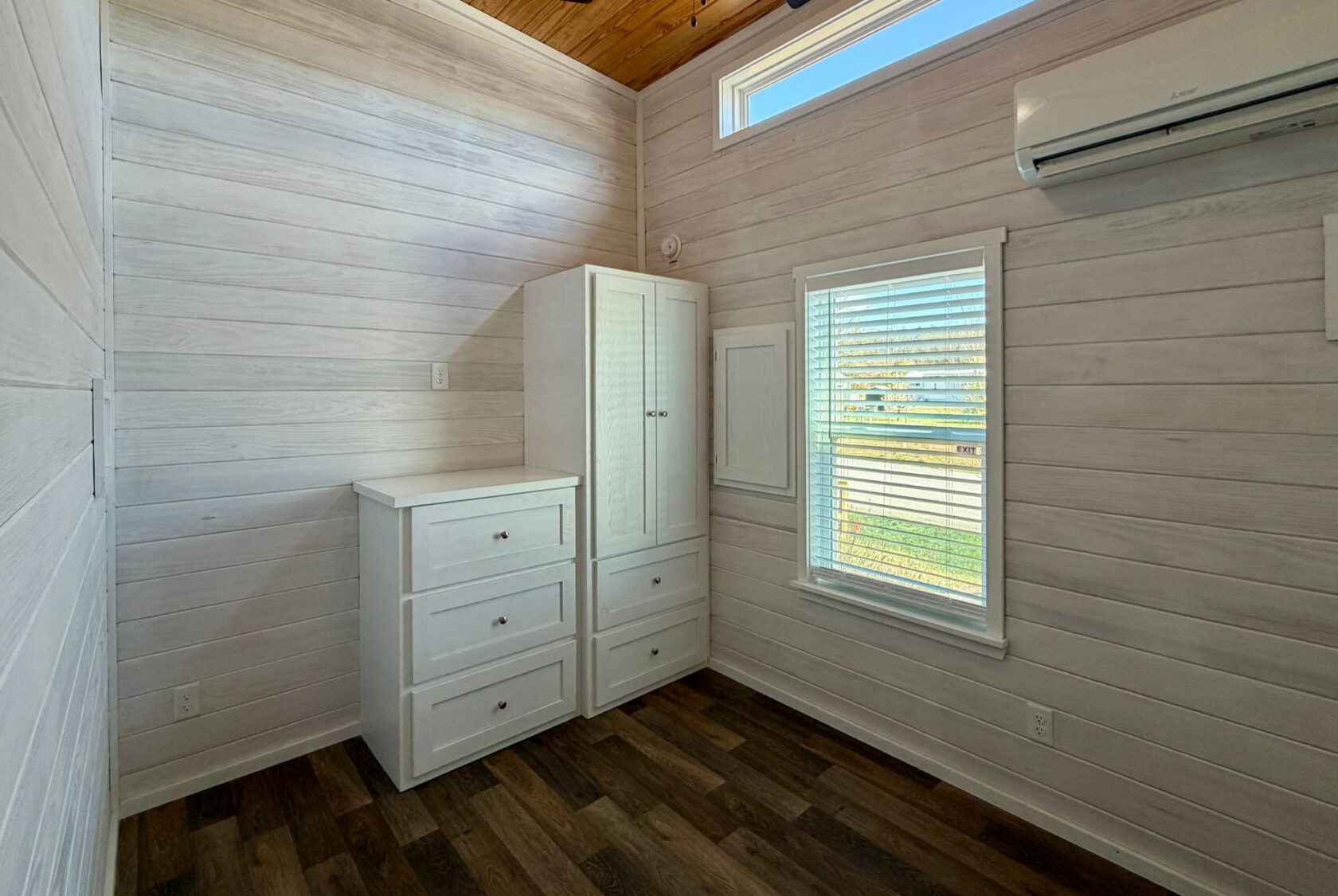 Small, bright room on Breezy Meadow Lane with white wood walls, dresser, wardrobe, window, and wall-mounted air conditioner.