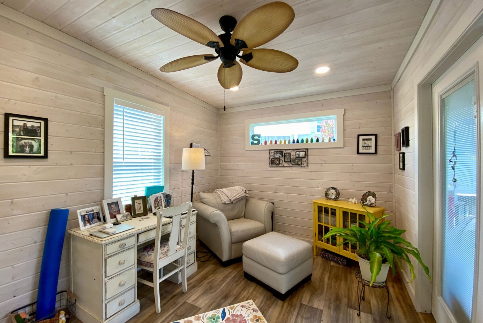 Cozy sunlit room on Easy Lane with white walls, desk, armchair, ottoman, yellow cabinet, and green plant.