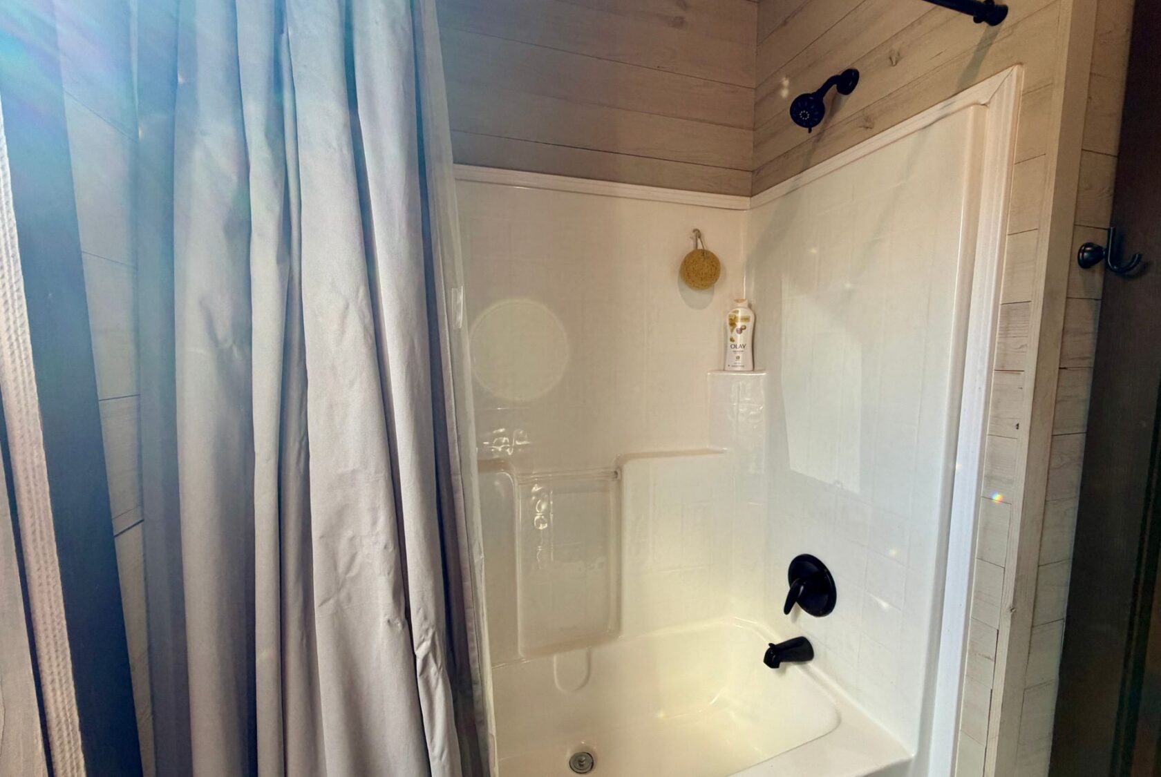 White bathtub and shower with a curtain, black fixtures, and wood-paneled walls at 31 Rest Awhile Lane.