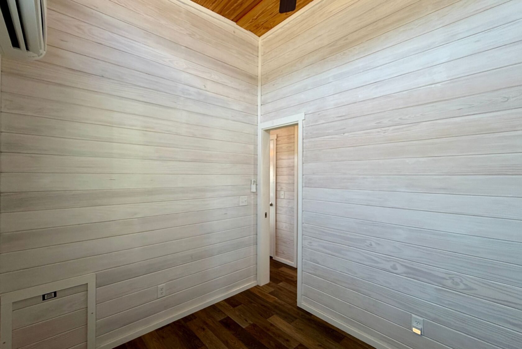 Empty room with white wood panel walls, wooden floor, and a door—perfect for Breezy Meadow Lane living.