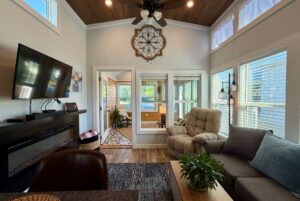 Bright living room at 106 Meandering Lane with large clock, armchair, wall-mounted TV, and windows letting in natural light.