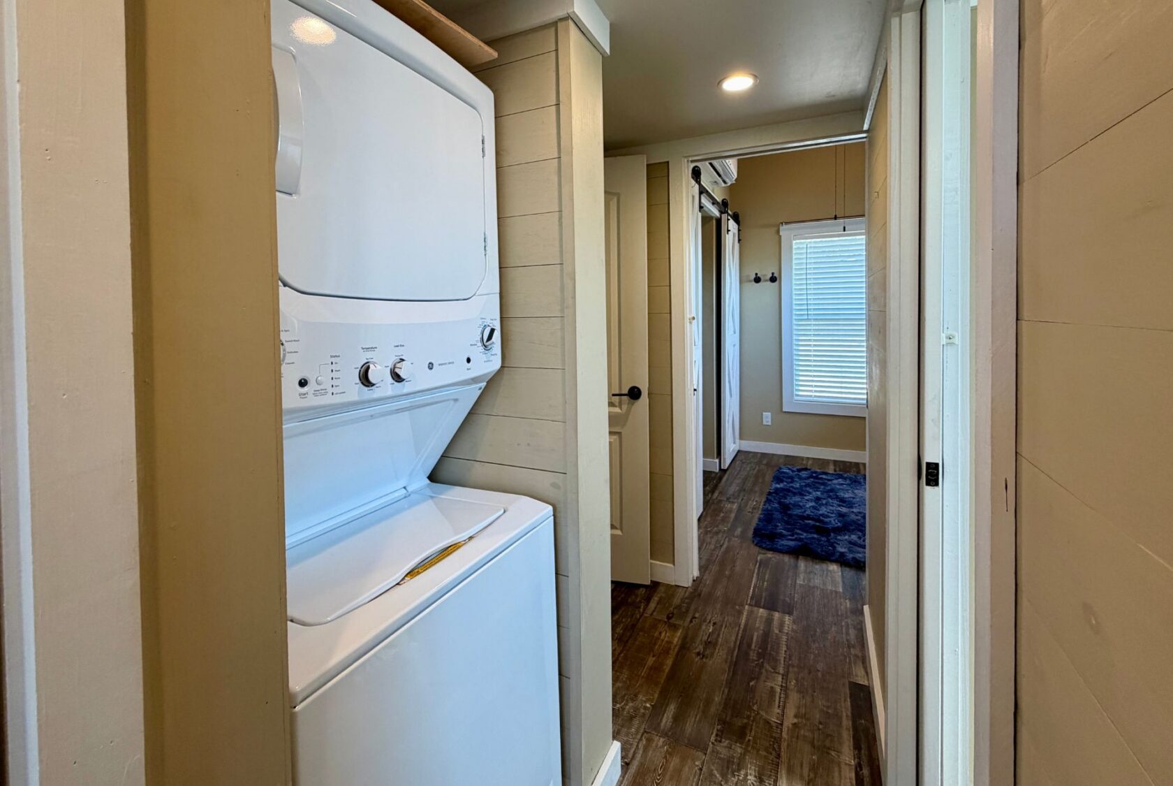 Stacked washer and dryer in a small laundry nook beside the 53 Highland Hill hallway with wooden floors and beige walls.