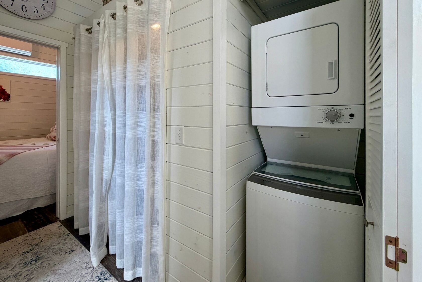 Stacked washer and dryer in a cozy laundry nook at 47 Drifting Brook, next to a bedroom with white shiplap walls.