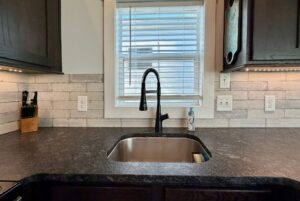 A modern kitchen sink at 106 Meandering Lane features a black faucet, soap dispenser, and white tile backsplash.